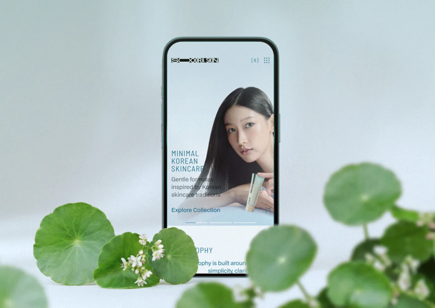 Soora Skin homepage on a phone, surrounded by green centella leaves
